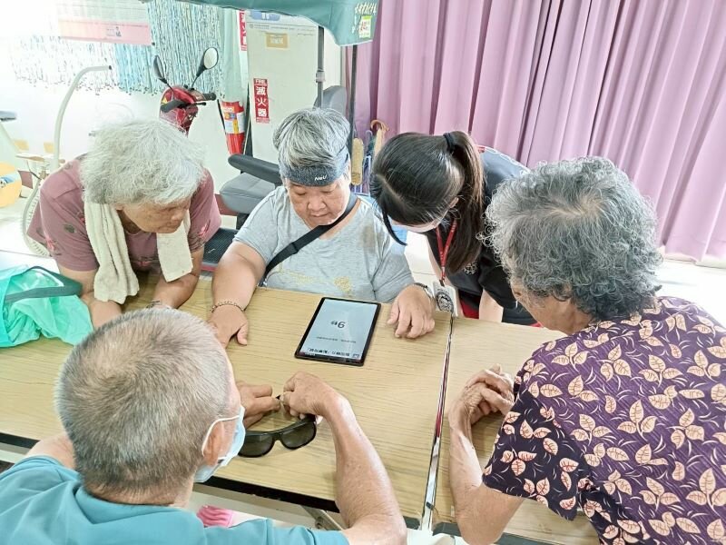 長者們圍坐在平板前，共同參與數位認知遊戲，提升專注力與團體互動。(圖片來源/敏惠醫護管理專科學校)