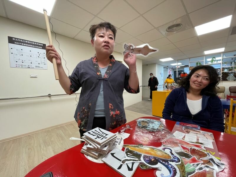 業務負責人李秀涵展示他設計的釣魚遊戲等自製教具。（攝影/戴淨妍）
