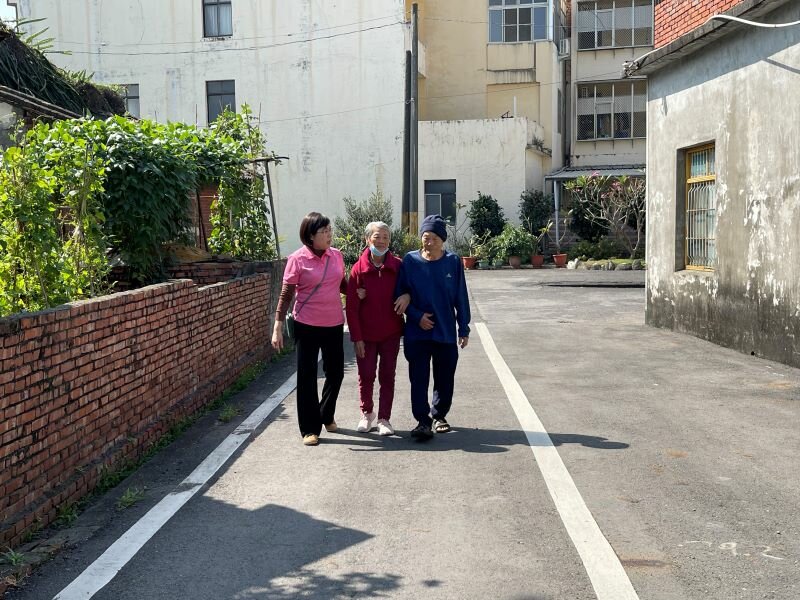 如果長輩沒有足夠的力氣支撐身體，就無法有效進行吞嚥肌群訓練。圖中民暉居家護理所所長郭美伶與陳阿公、陳太太，一起在家門口練習走路。(攝影/戴淨妍)