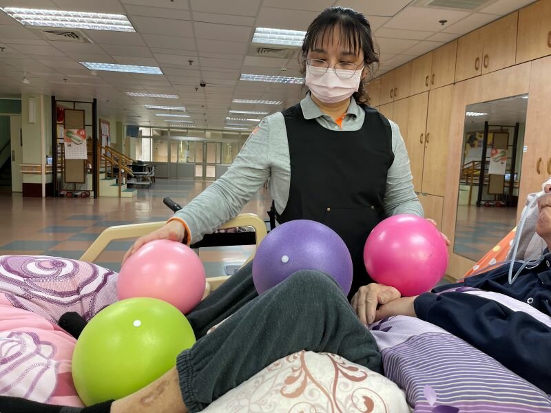 松柏園的照服員協助中風的李伯伯做執行口腔機能復甦，用彈力球協助擺位。(攝影/戴淨妍)